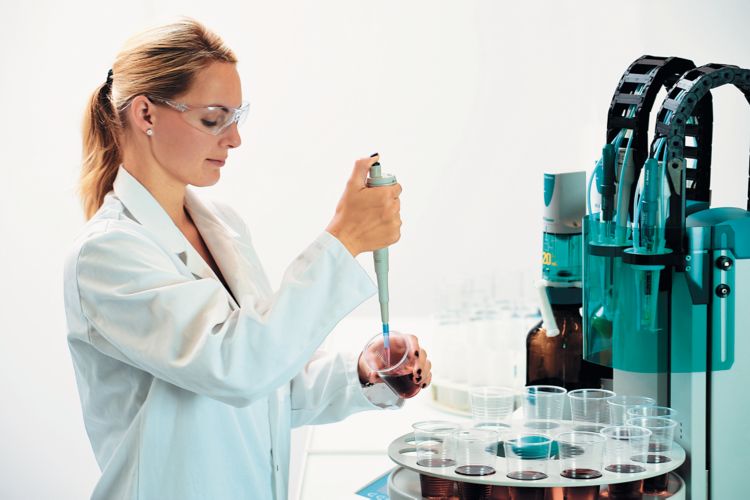 Female operator standing close to the automated system pipetting into a beaker with sample. Image with lab personnel from 814 USB Sample Processor brochure (document nr. 88145001) or 815 Robotic USB Sample Processor XL brochure (document nr. 88155001)