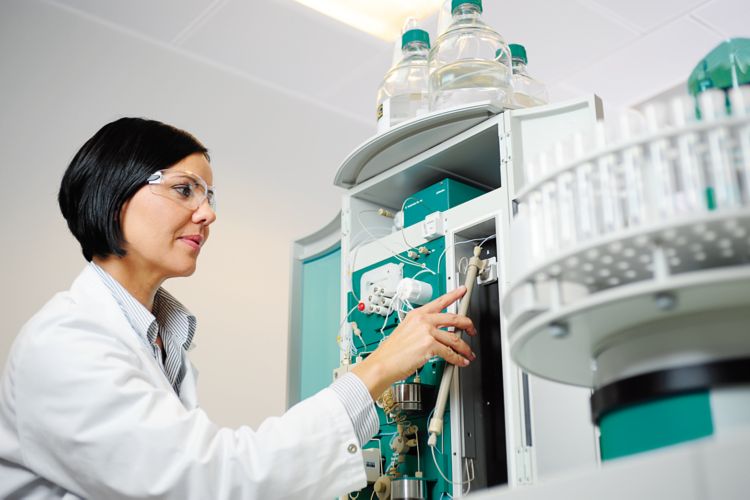 woman in laboratory with ion chromatograph in the background and an IC column in the hand