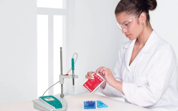 Woman in lab coat opening a pH buffer, pH meter in front of her