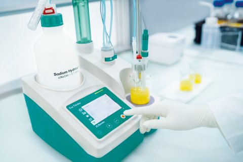 Titulador compacto Eco KF Titrator com uma mão com luva apertando o botão do equipamento.