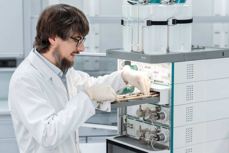 woman in laboratory with ion chromatograph in the background and an IC column in the hand