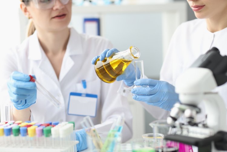 Two researchers in laboratory examine golden liquid in test tube. Laboratory diagnostics concept