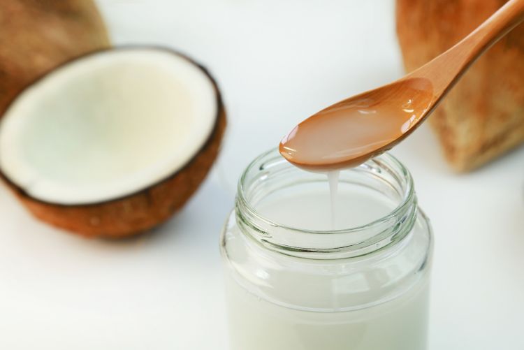 Close-up photo of a spoonful of opaque white coconut oil dripping into a glass jar.