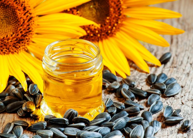 Sunflower oil in a jar with sunflower seeds scattered around and two sunflowers behind it.