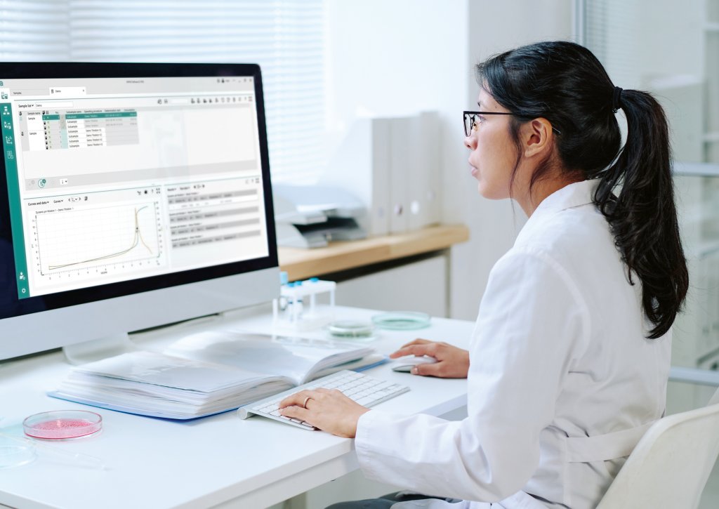 Young Hispanic female virologist with dark long hair studying new virus while sitting by desk in front of computer in laboratory