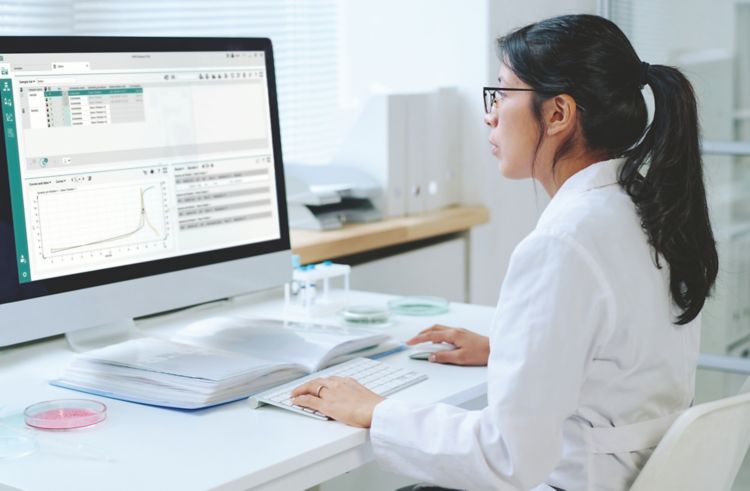 Young Hispanic female virologist with dark long hair studying new virus while sitting by desk in front of computer in laboratory