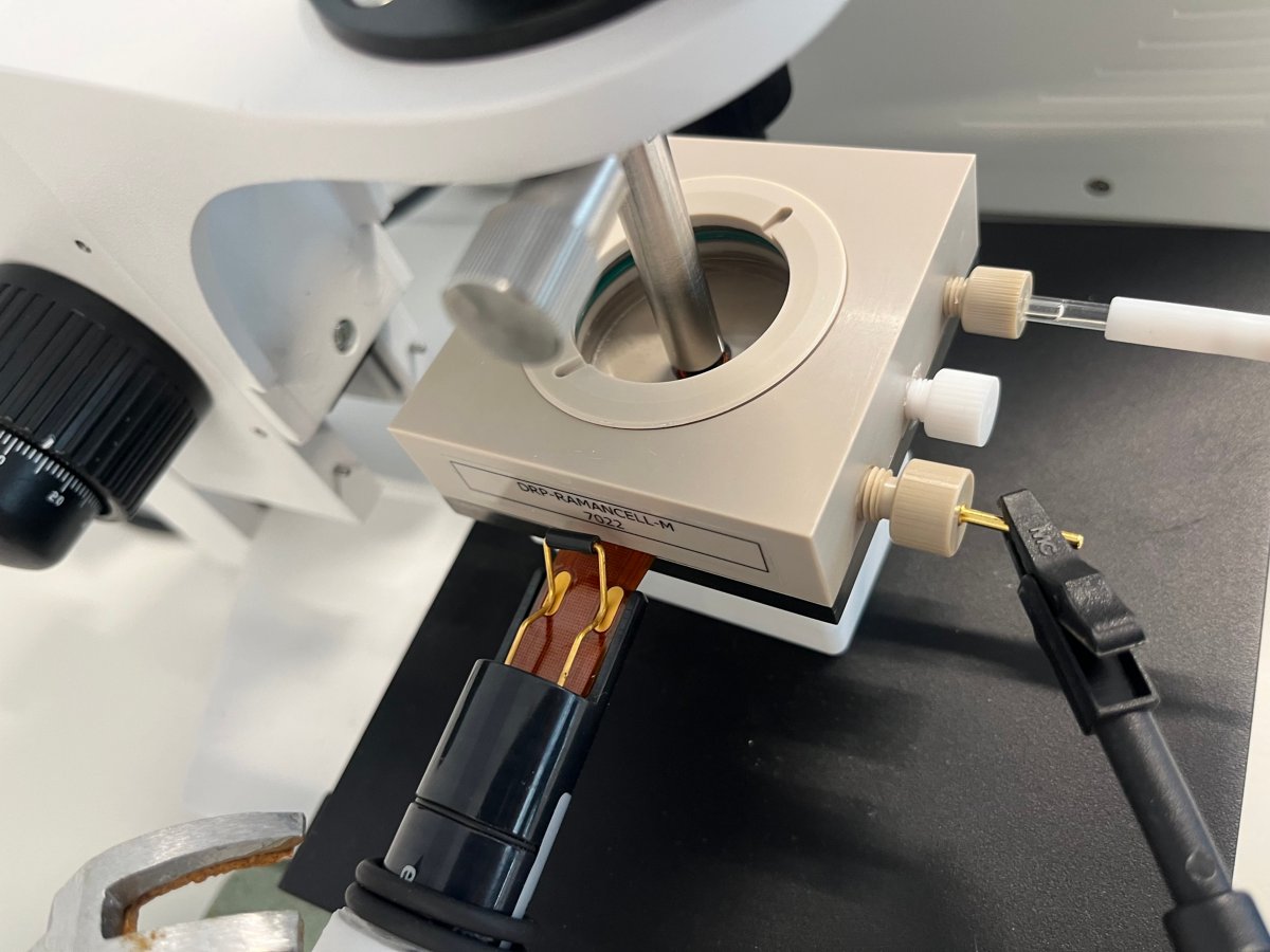 Célula EC-Raman com a sonda Raman e o suporte da sonda no centro. Nas laterais da célula, são visíveis os eletrodos e a sonda de EQCM-D.
