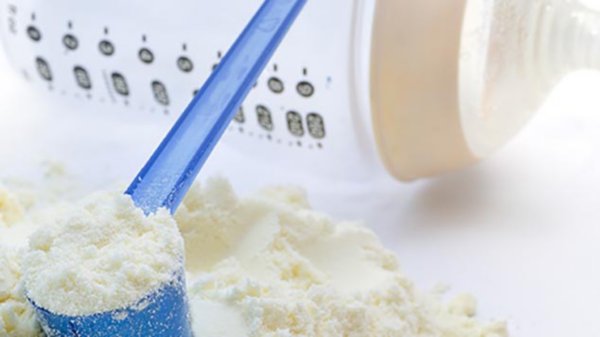 A close-up shot of baby milk formula with a plastic measuring spoon and bottle.